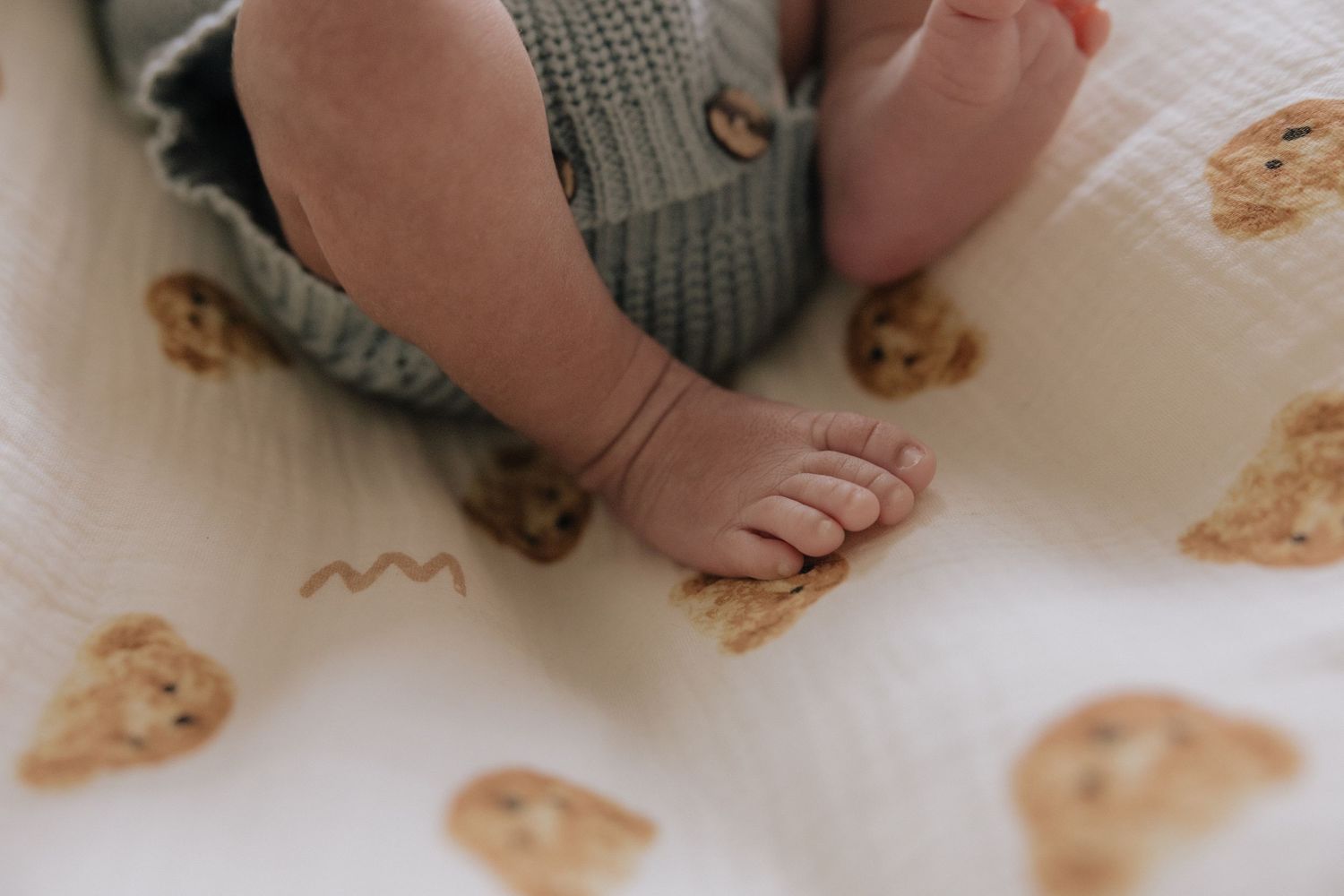Close-up of newborn baby feet on a white muslin swaddle blanket with cute teddy bear and cookie prints.