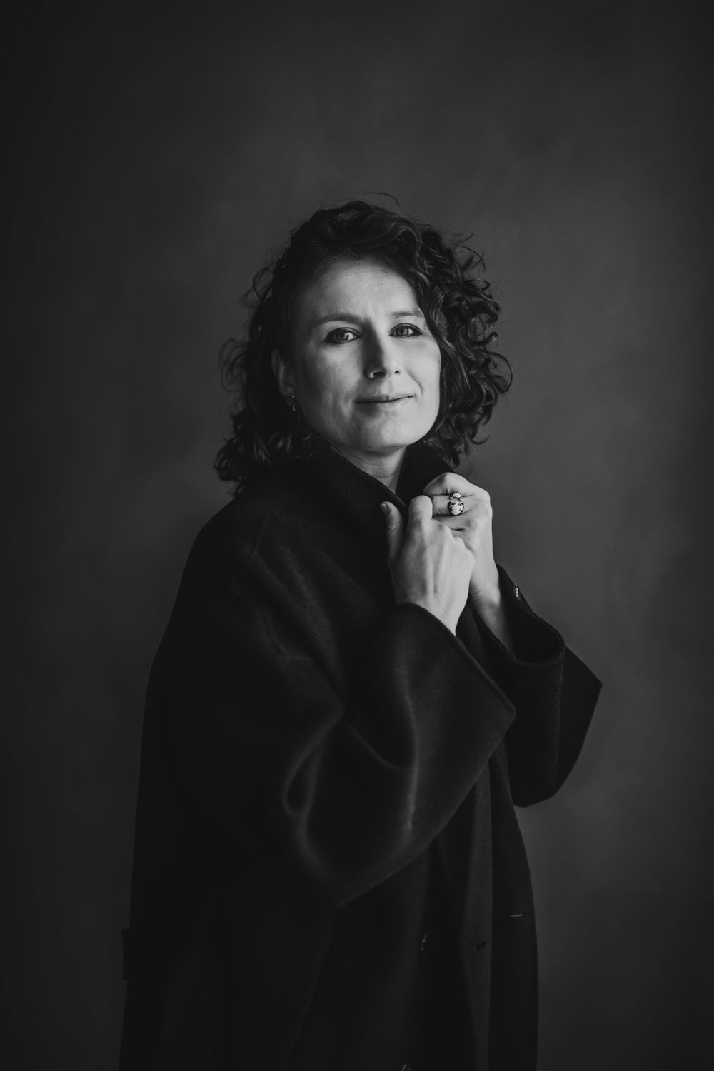 Classic portrait in oversized coat with natural curls against dark backdrop. Bellevue studio, WA