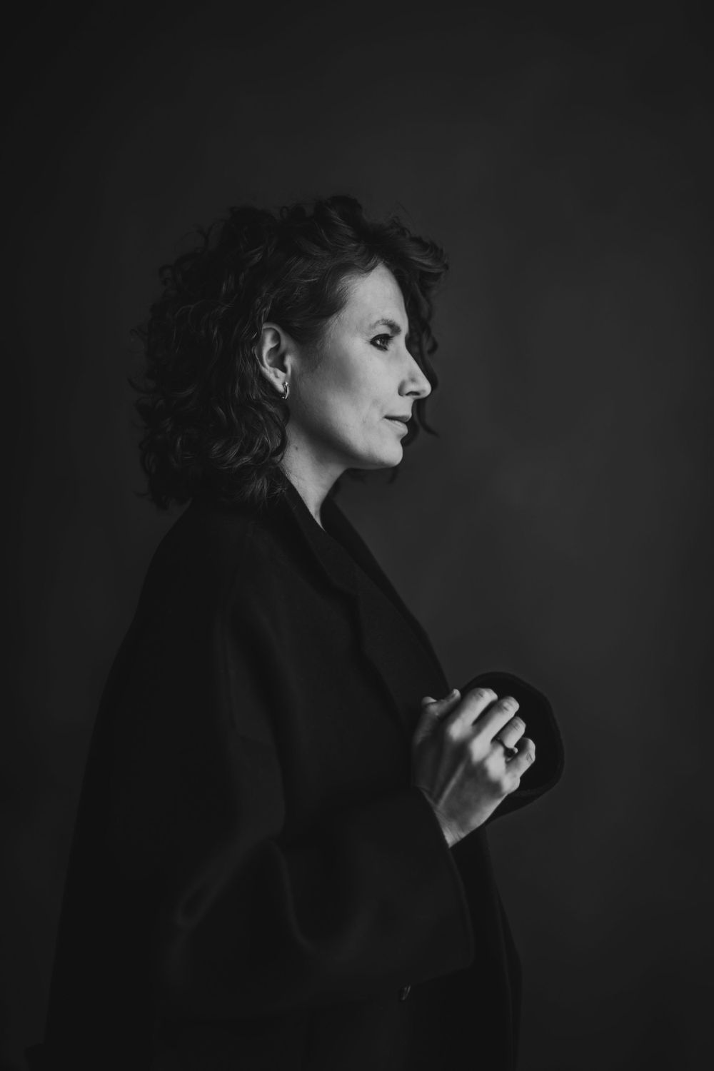 Side profile artistic portrait featuring dark coat and expressive pose against black background. Bellevue studio, WA