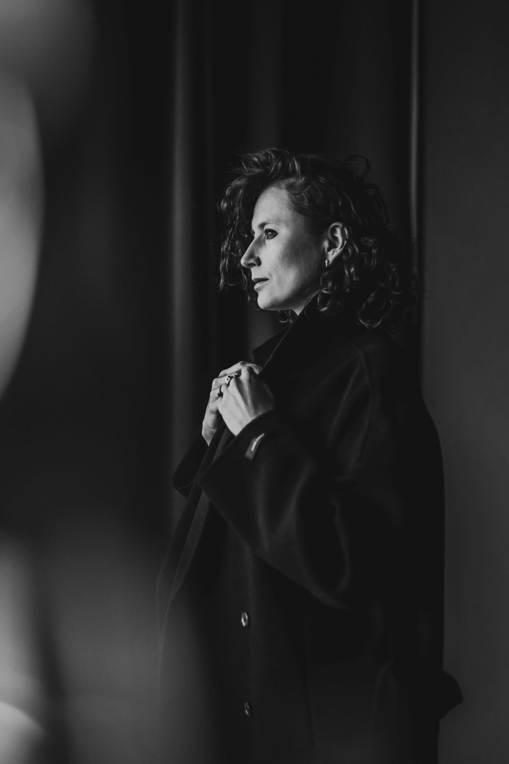 Dramatic black and white portrait of a woman in dark coat with curly hair against moody lighting. Bellevue studio, WA