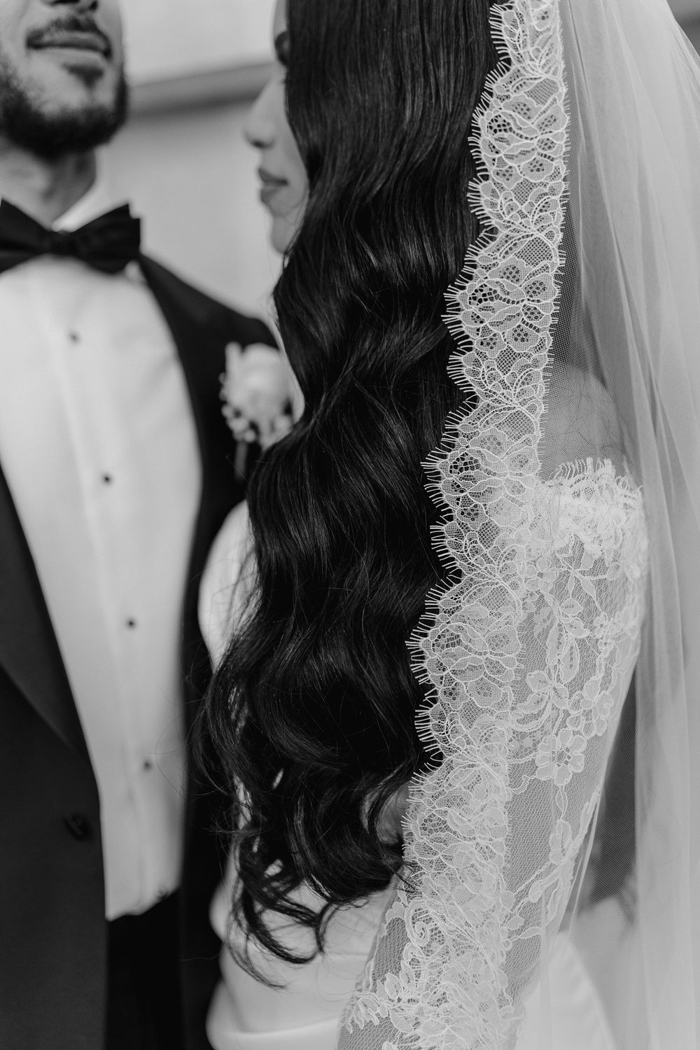 Close-up of intricate lace veil and wavy dark hair against formal attire.