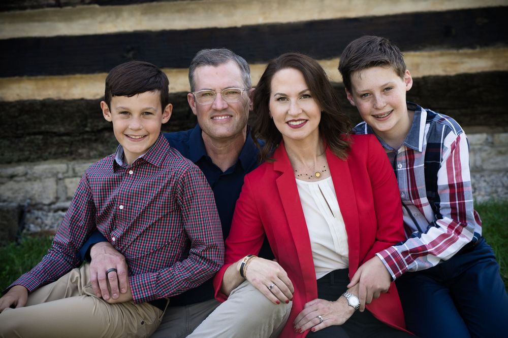 A happy family of four poses outdoors, with two boys flanking their smiling parents in a warm portrait.