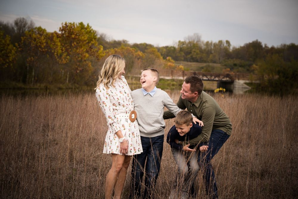 Family of four laughing together in an autumn field during an outdoor portrait session.