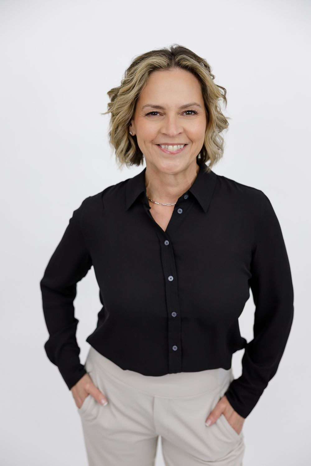 female business owner coach for corporate headshot against white background smiling with hands in pockets of pants in Bellevue, WA