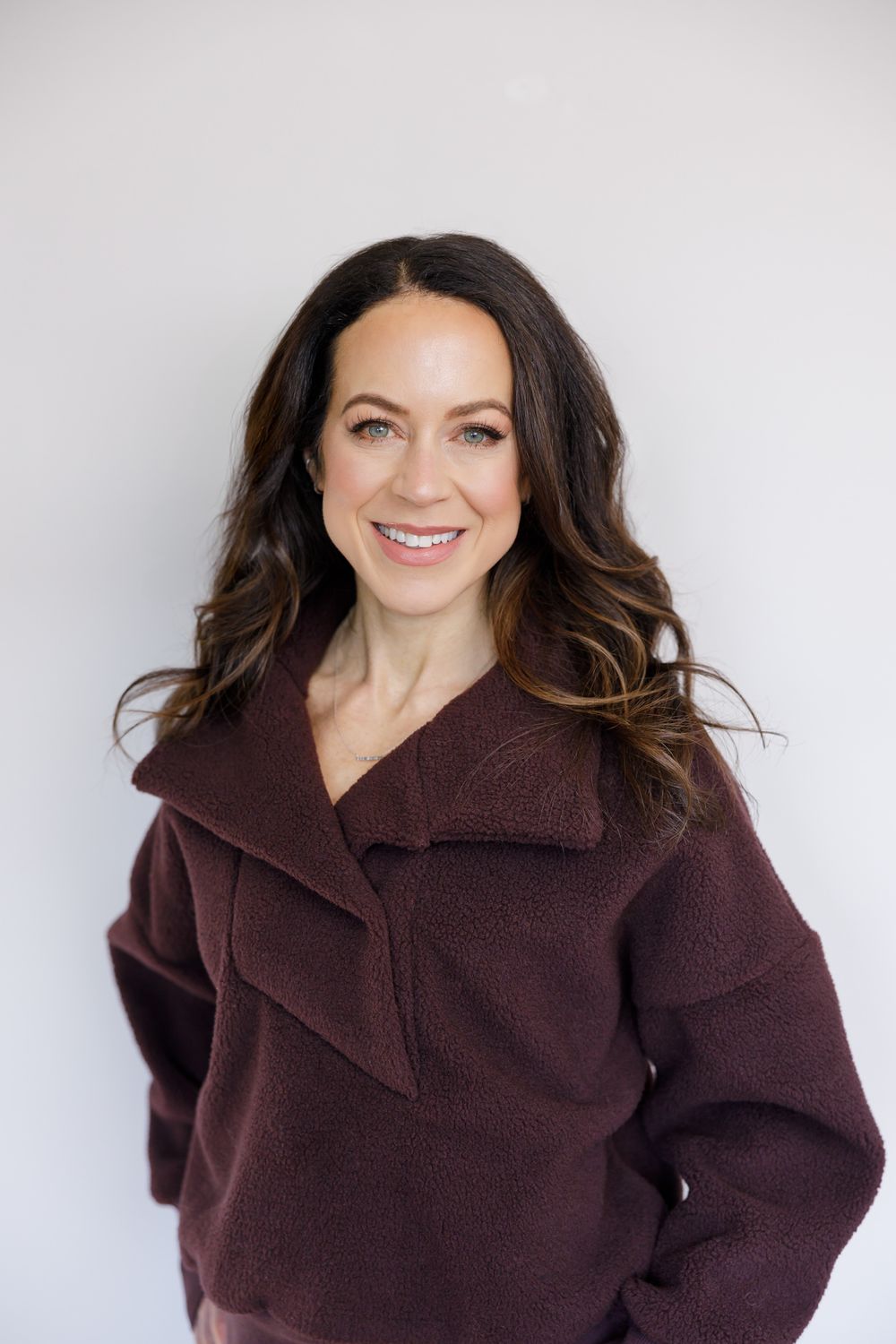 female personal trainer business owner in Seattle, WA standing against white backdrop for headshot smiling in dark red sweater