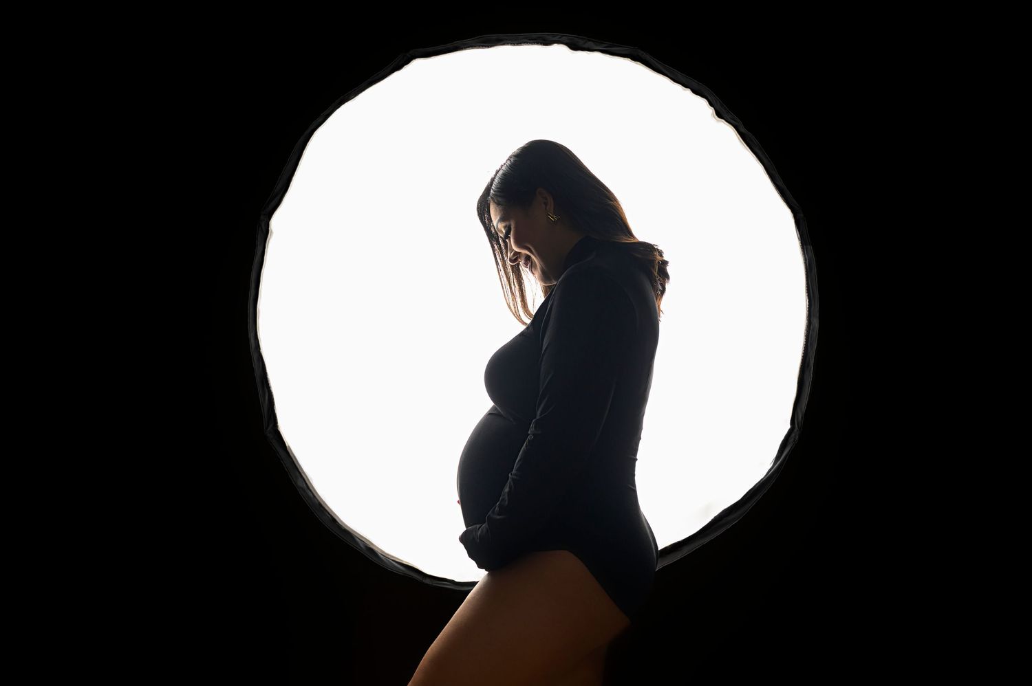 Artistic silhouette maternity photos against bright circular backlight.