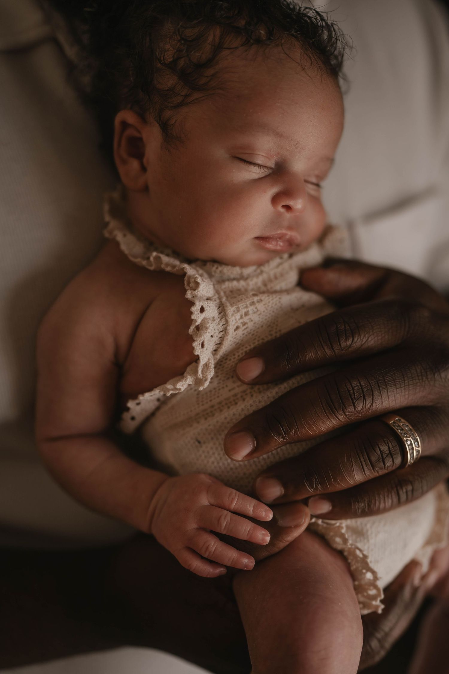 Palm Beach sleeping newborn baby in lace wrap held by caring hands in soft lighting.