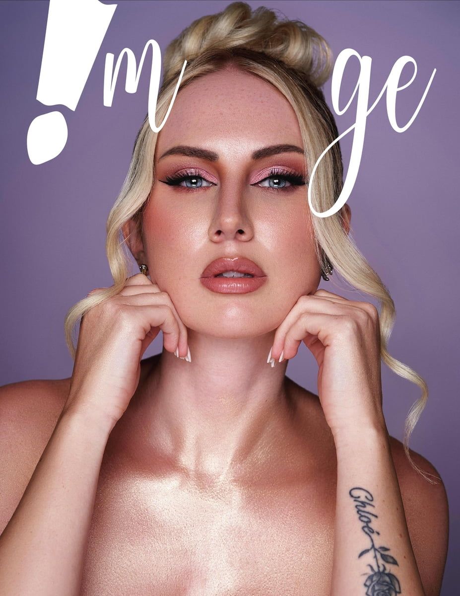 Beauty portrait with glamorous makeup, blonde wavy hair, and visible arm tattoo against purple background.
