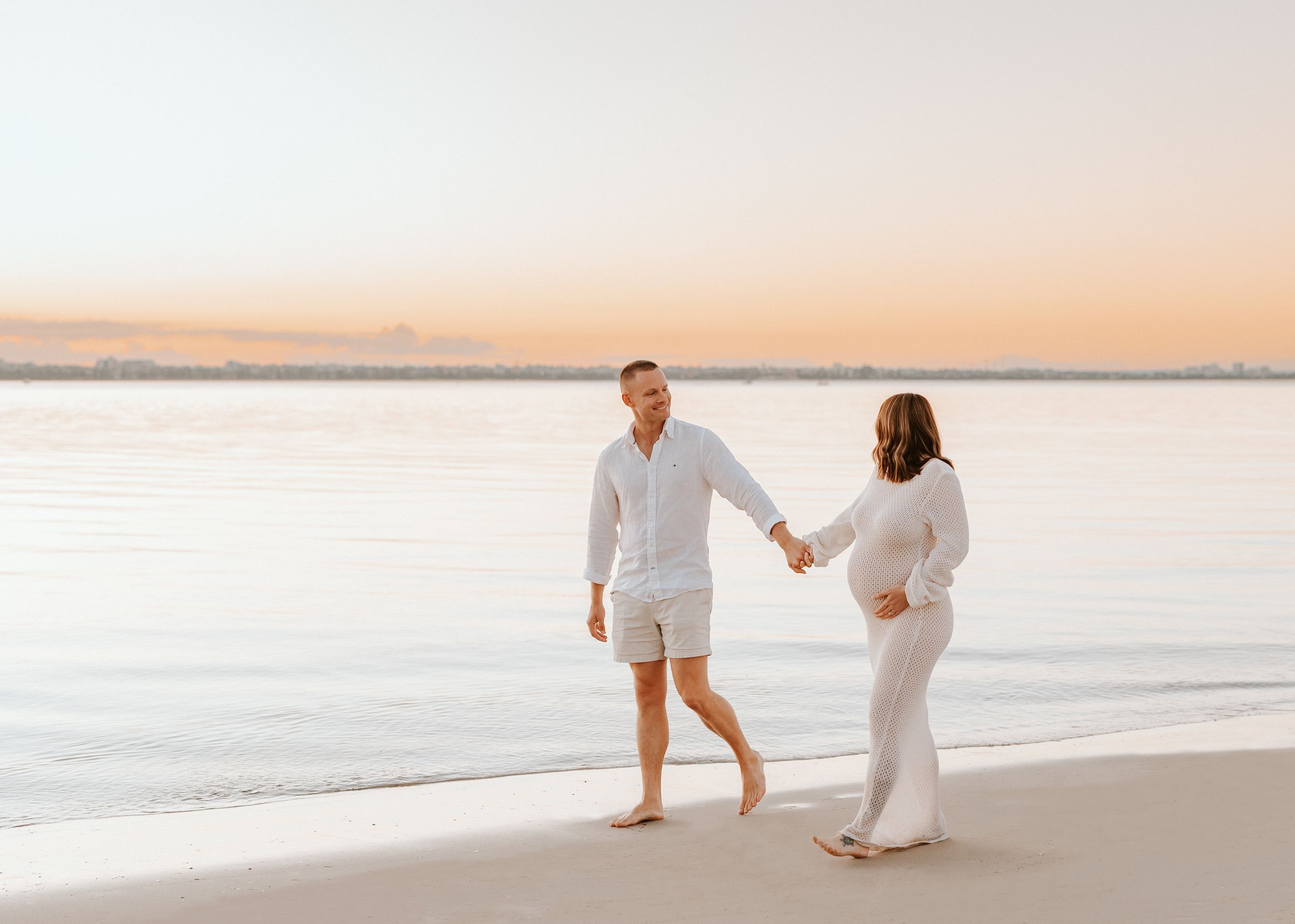 Couple walking at sunset during maternity session