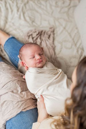 Sleeping newborn wrapped in white swaddle rests peacefully on beige blanket during a lifestyle newborn session in Springfield, MO.