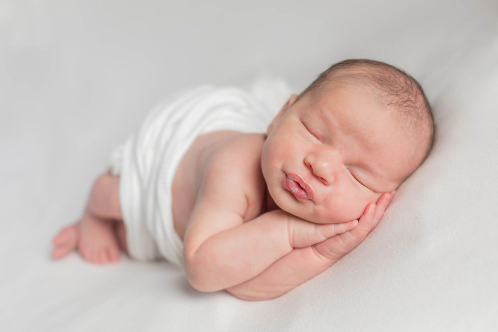 Peaceful newborn baby sleeping in white wrap on soft white backdrop during a lifestyle newborn session in Springfield, MO.