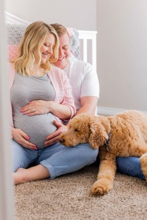 An expectant couple sits with their goldendoodle dog on carpeted floor during maternity photoshoot in Springfield, MO.