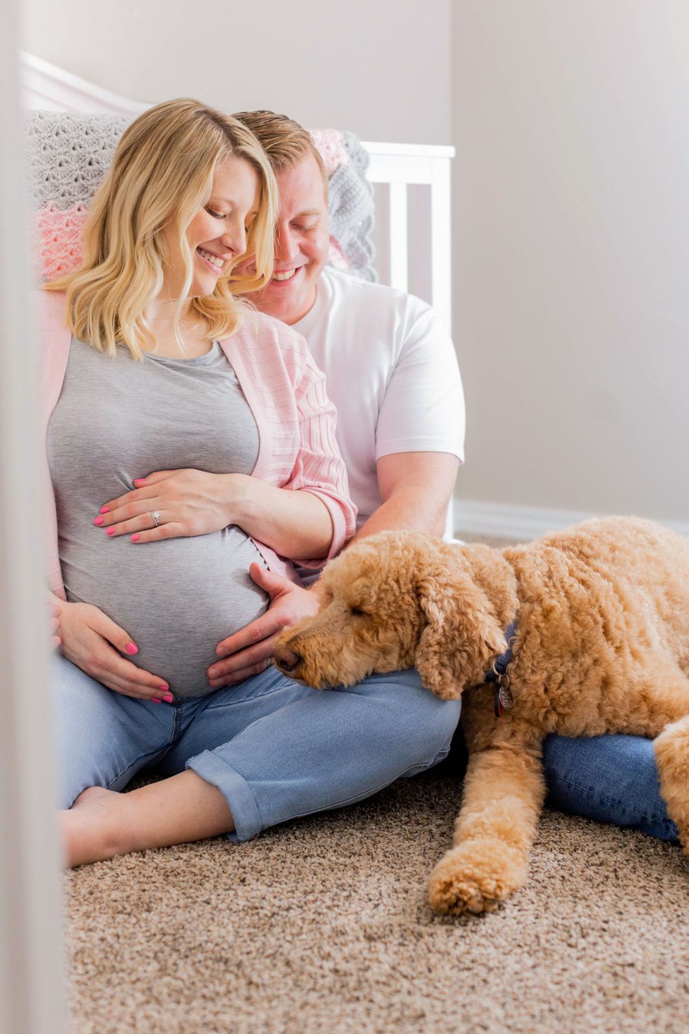An expectant couple sits with their goldendoodle dog on carpeted floor during maternity photoshoot in Springfield, MO.