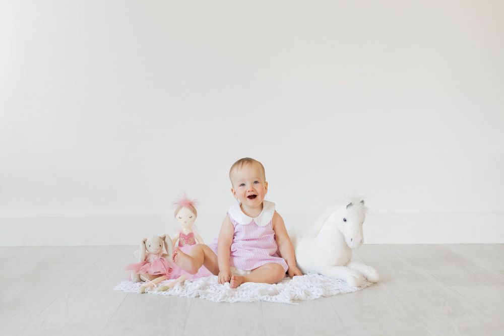 A baby sits on white fabric with stuffed animal toys during a lifestyle milestone session in Springfield, MO.
