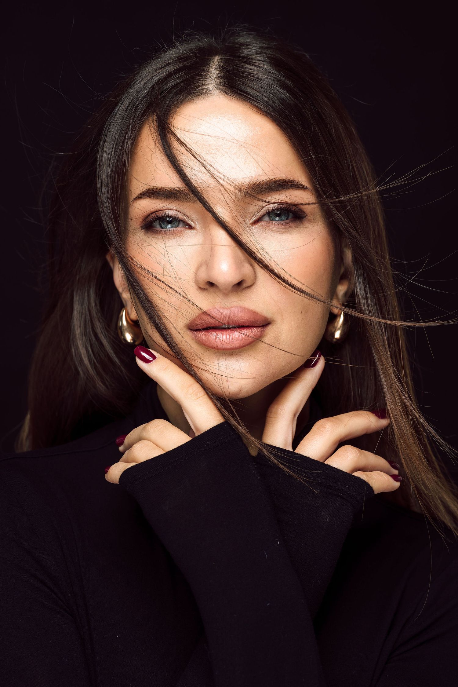 Portrait of woman in black turtleneck with dramatic lighting and windswept hair.