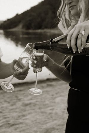Hands pouring champagne into glasses in black and white photography.