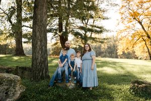 A family sits together on a grassy hill during golden hour with sunlight filtering through trees.