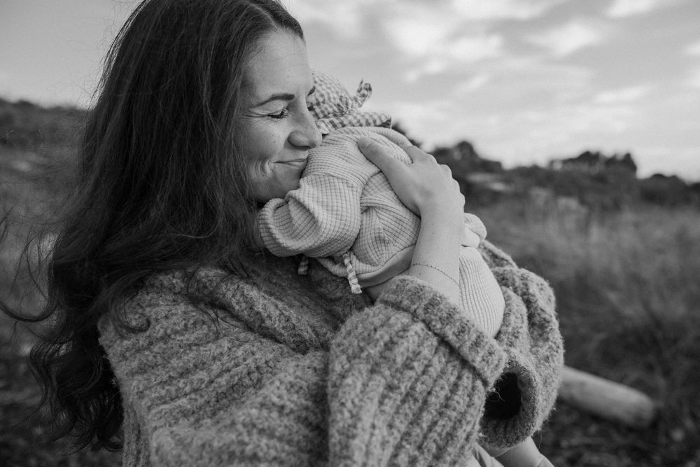 A series of black and white photos showing tender moments between a parent and baby in natural outdoor settings.
