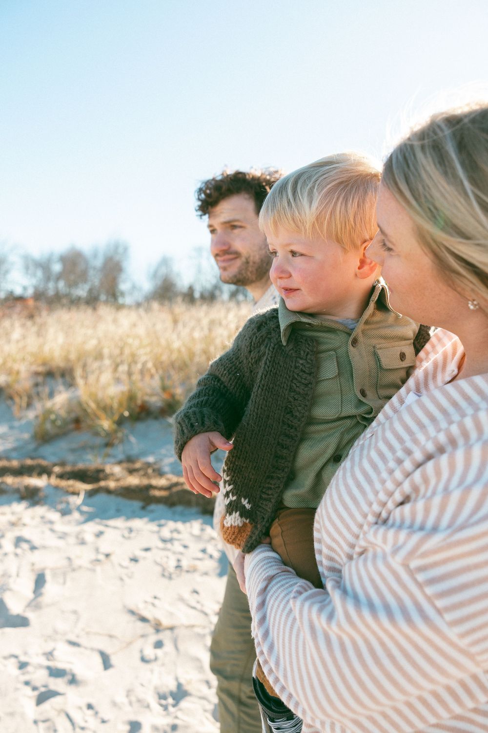 Family enjoying a tender moment together on a sandy beach during golden hour.