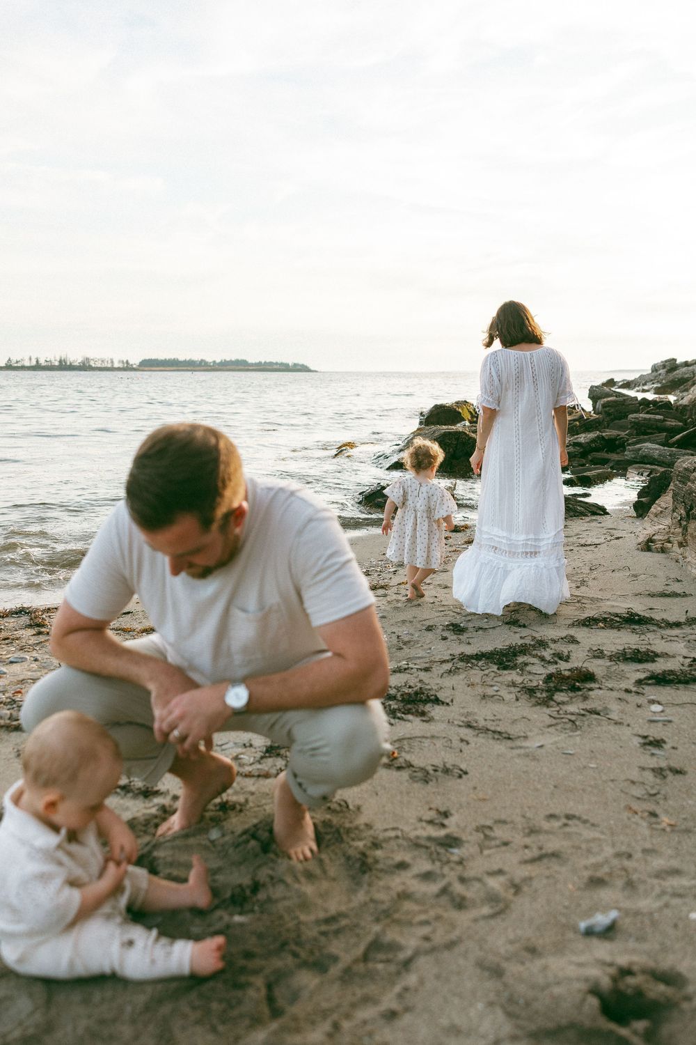 Family exploring and playing together on a peaceful beach at sunset.