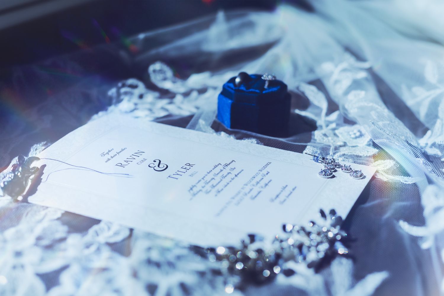 A diamond halo engagement ring and wedding band displayed in a blue velvet octagonal ring box on a dark wood surface.