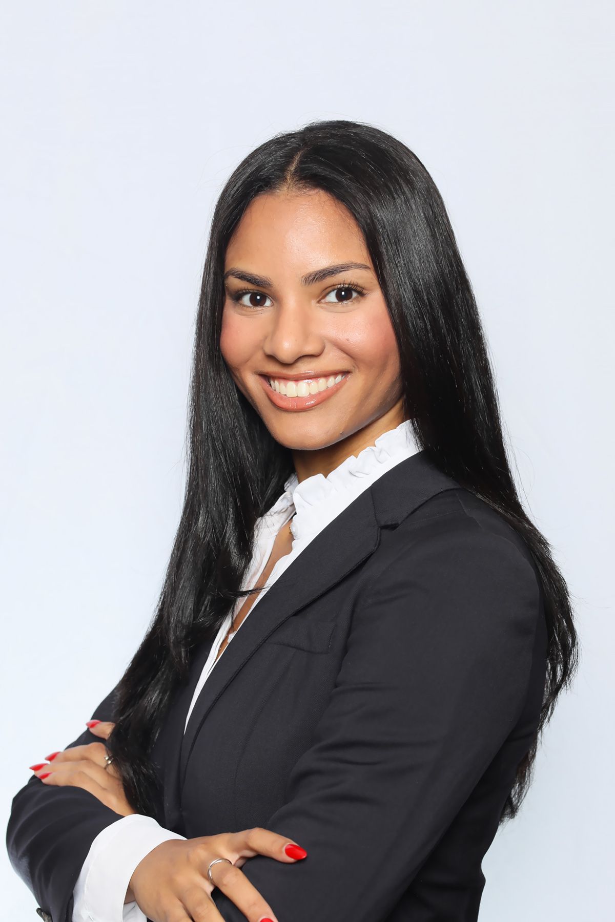 Smiling businesswoman in black blazer and white blouse with arms crossed against light blue background.