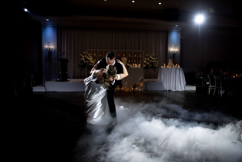 Groom dips bride during first dance surrounded by dramatic fog effects.