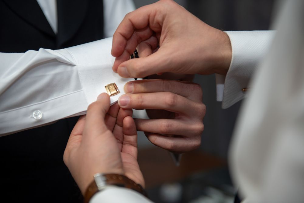 Close-up of hands fastening gold cufflinks on white dress shirt sleeve before wedding.