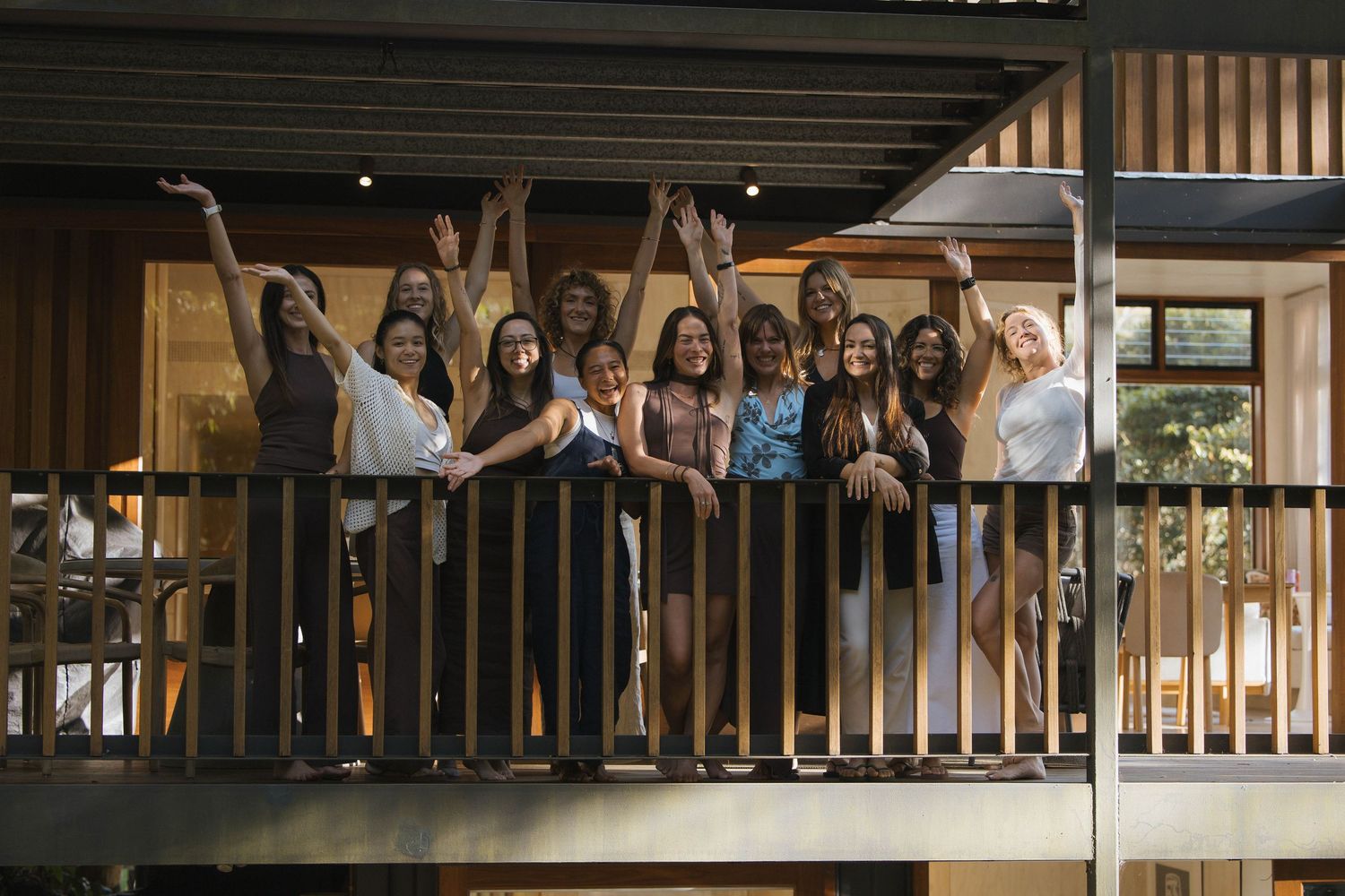 Group of cheerful women celebrating with raised arms on a balcony at an evening event.