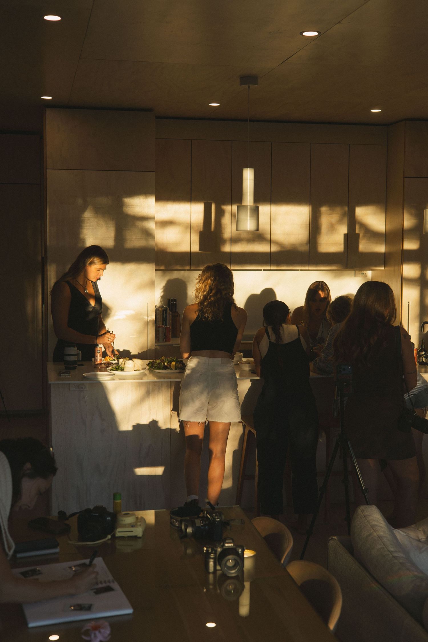 Women gathered around a kitchen counter in warm golden sunset light during an intimate indoor photography event.