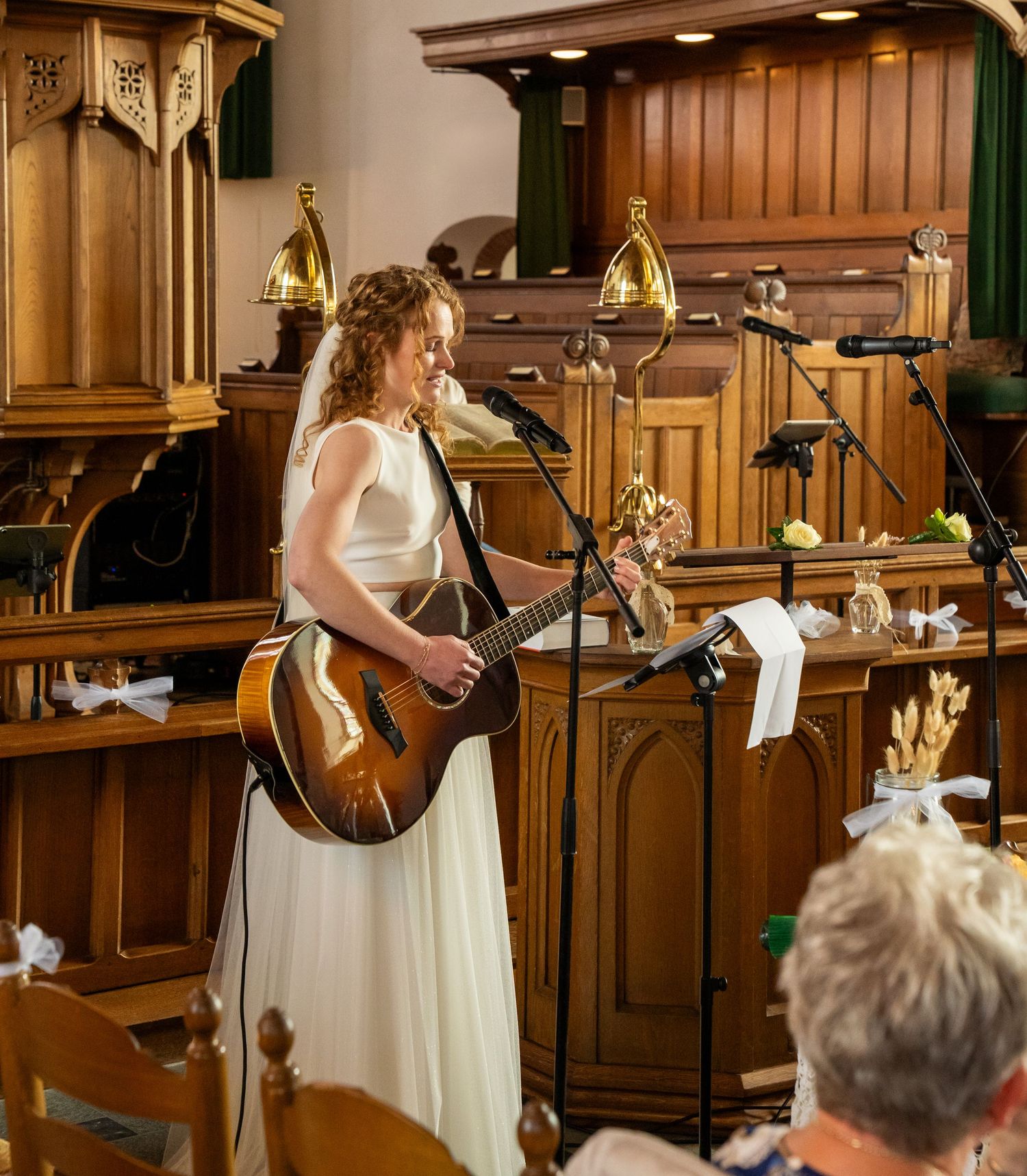 Bruid in witte jurk die akoestische gitaar speelt bij het altaar tijdens een kerkelijke huwelijksceremonie.