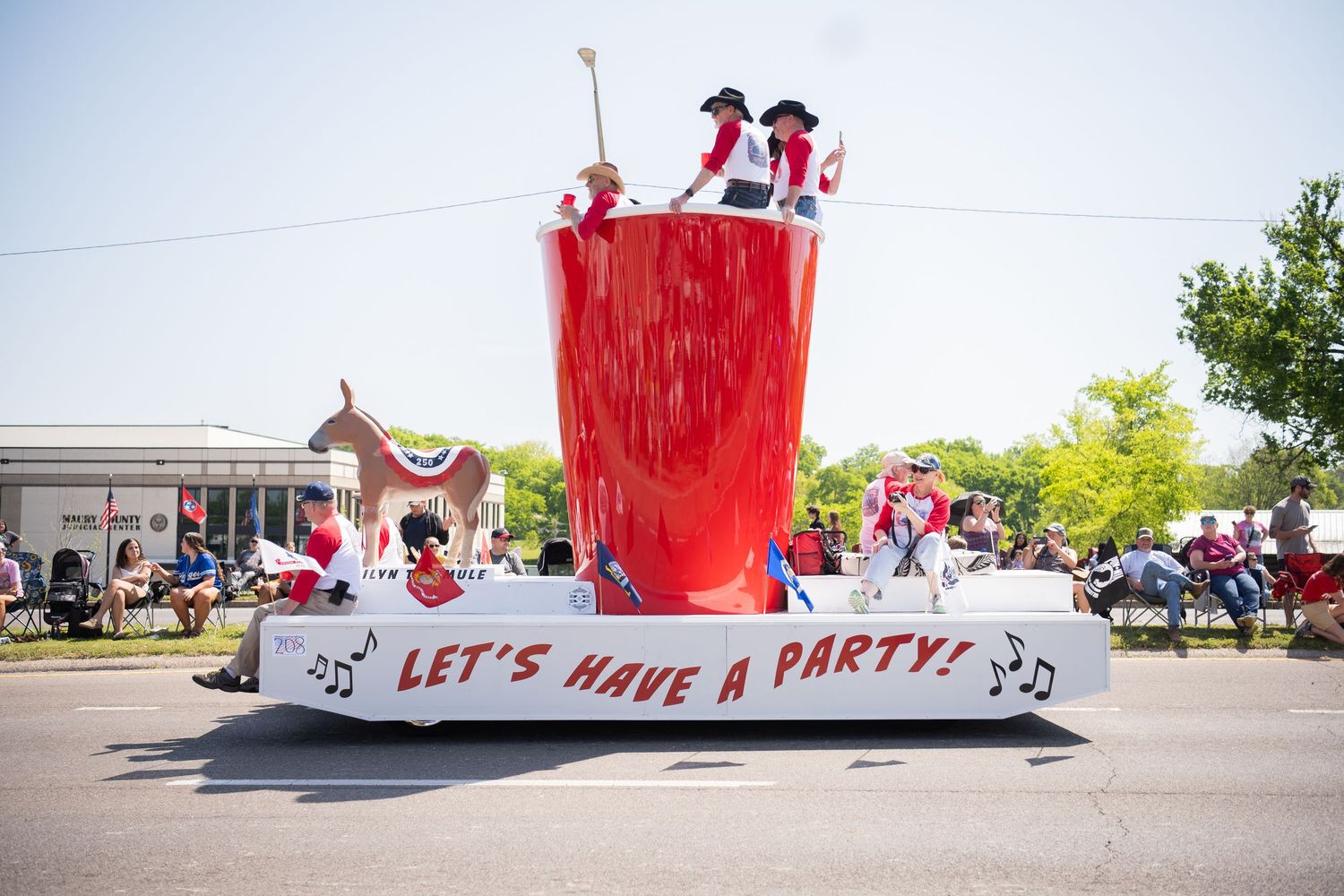 A festive parade float with a giant red cup and "Let's Have a Party!" banner, featuring performers in red costumes.