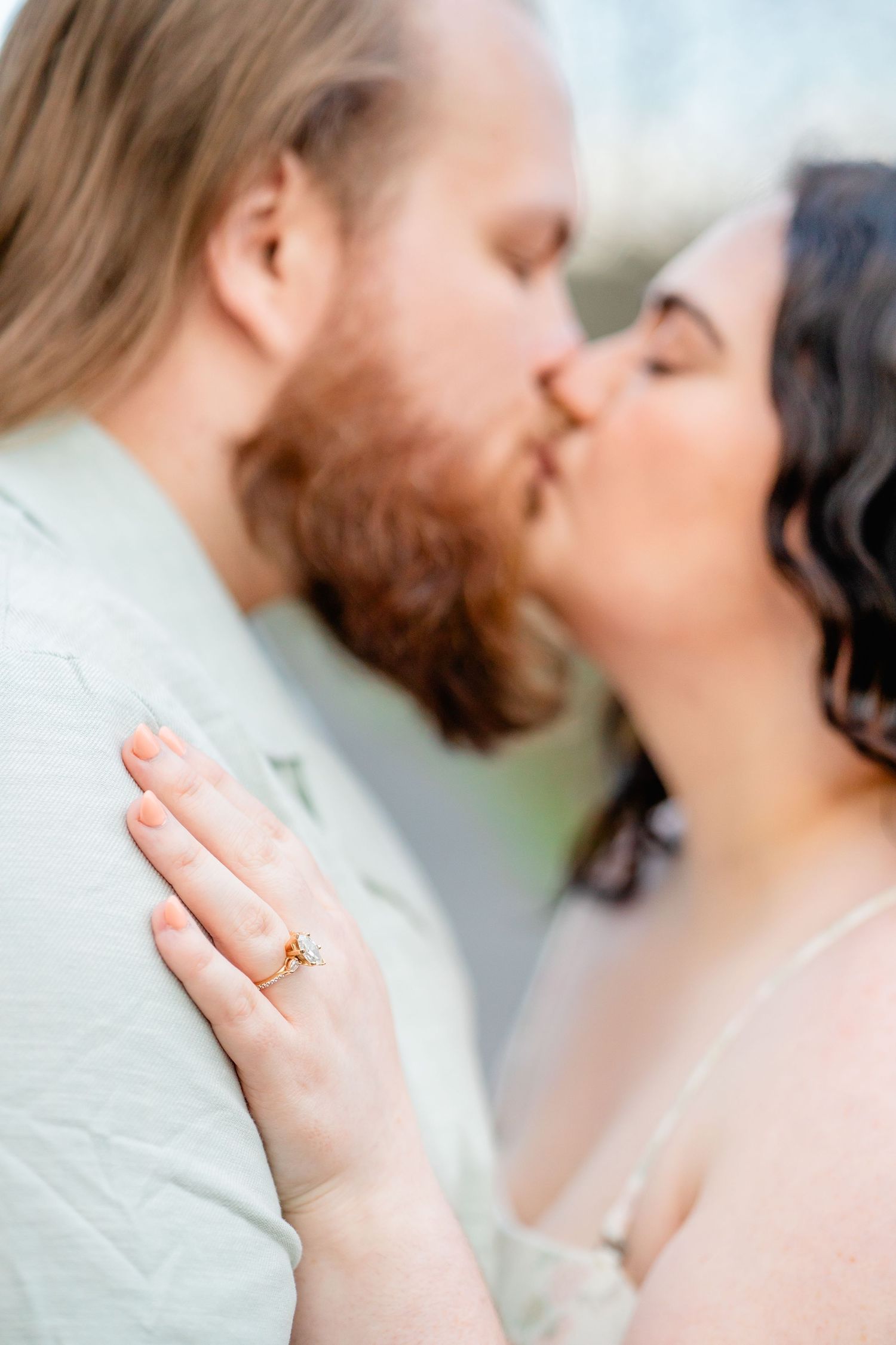 Close-up of a couple kissing, woman's hand with gold ring resting on man's chest, soft focus romantic portrait.