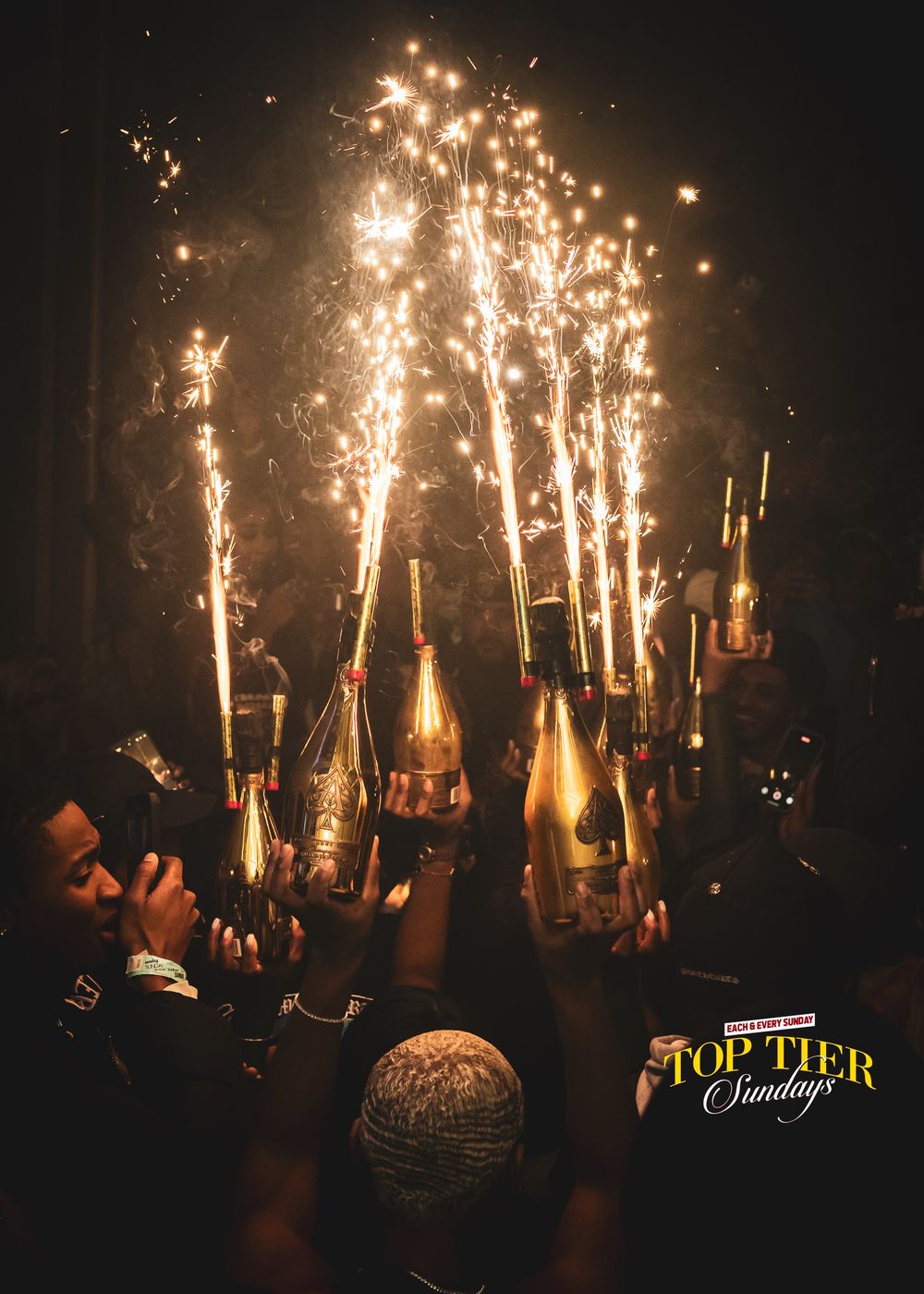 Champagne bottles with sparkler fountains held up by crowd at Top Tier Sundays nightclub celebration.