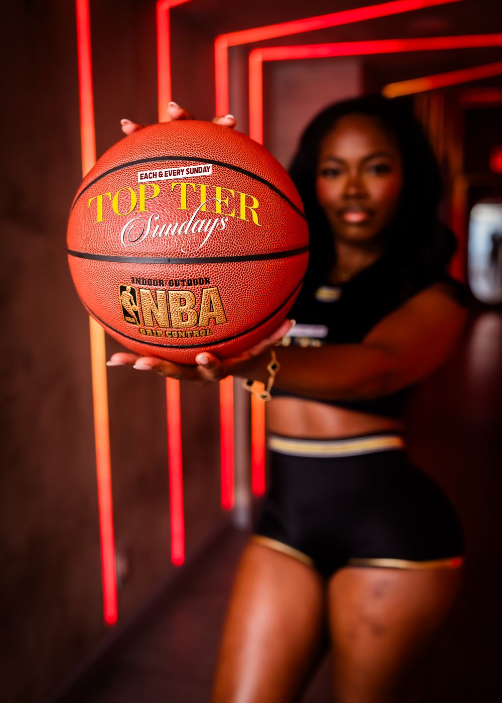 Woman holding NBA Top Tier Sundays branded basketball in neon-lit tunnel corridor.