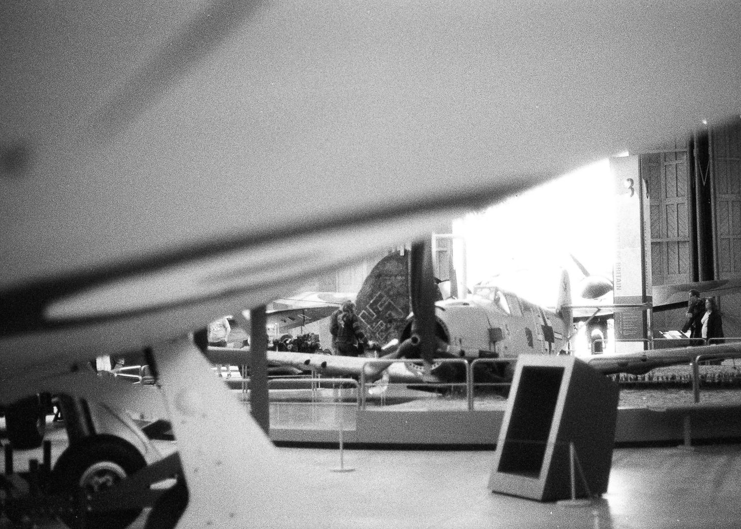 Black and white photo of vintage aircraft on display inside a museum hangar with informational signage.