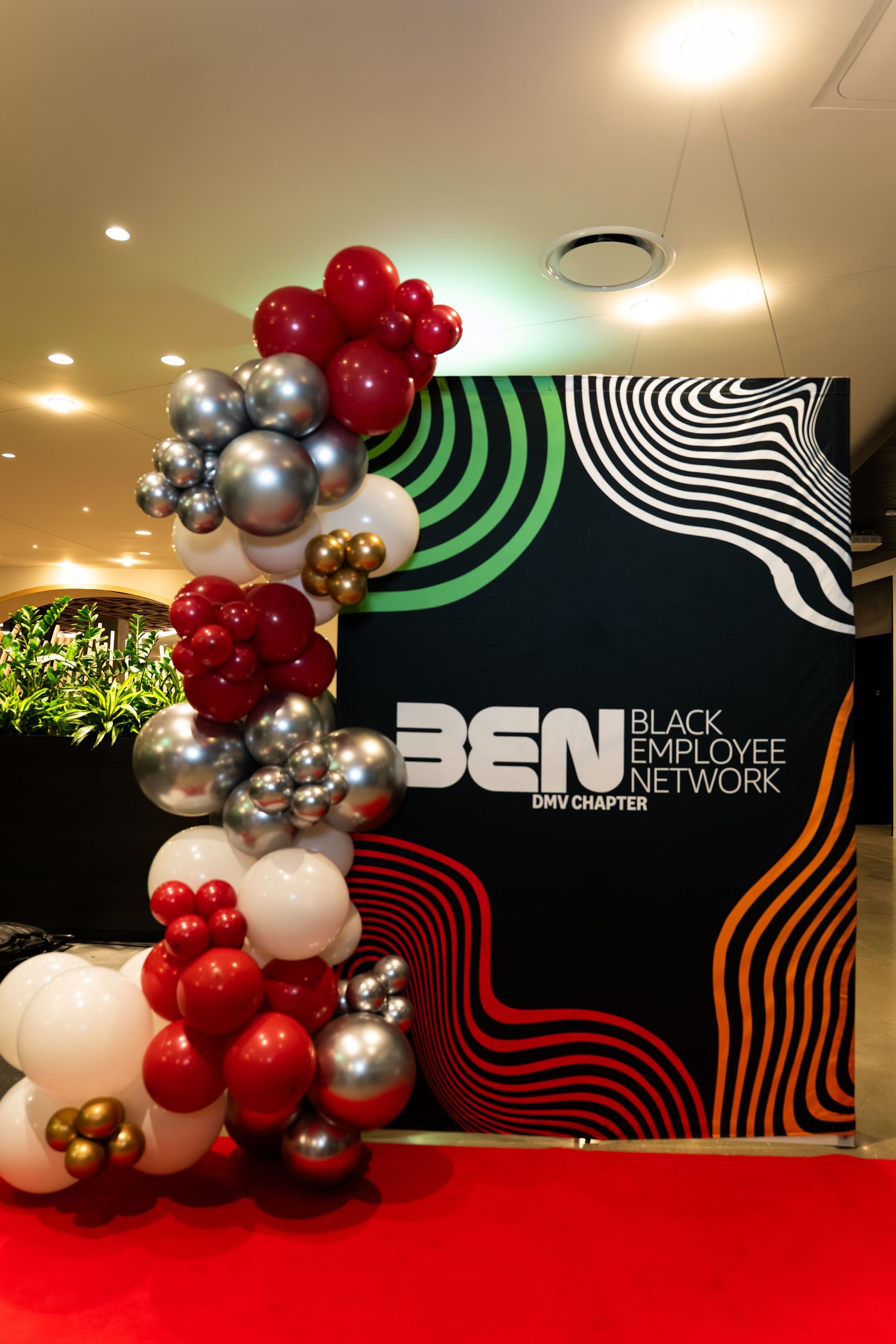 A modern corporate event space with red and silver balloon decorations against a black wall featuring the BCN logo design.