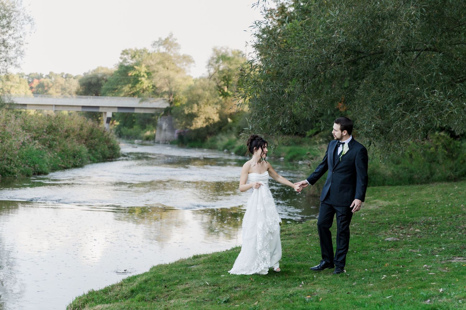 Wedding photography of Bride and groom holding hands walking along the grand river during sunset at The Wren House in St. Jacobs, Ontario.