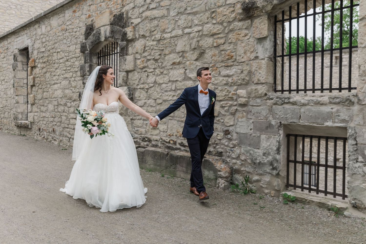 Bride and groom hold hands walking by goldie mill during their wedding overlooking their ceremony space in downtown guelph, Ontario.