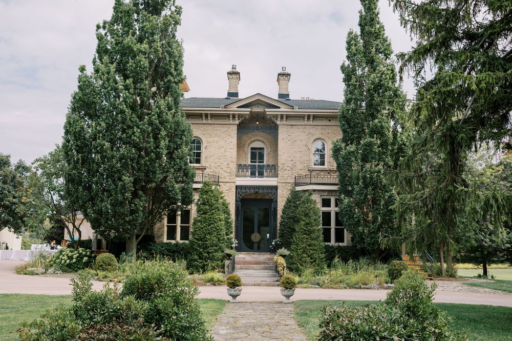 Elegant two-story brick mansion with tall cypress trees, manicured gardens, and a brick pathway leading to the grand entrance.