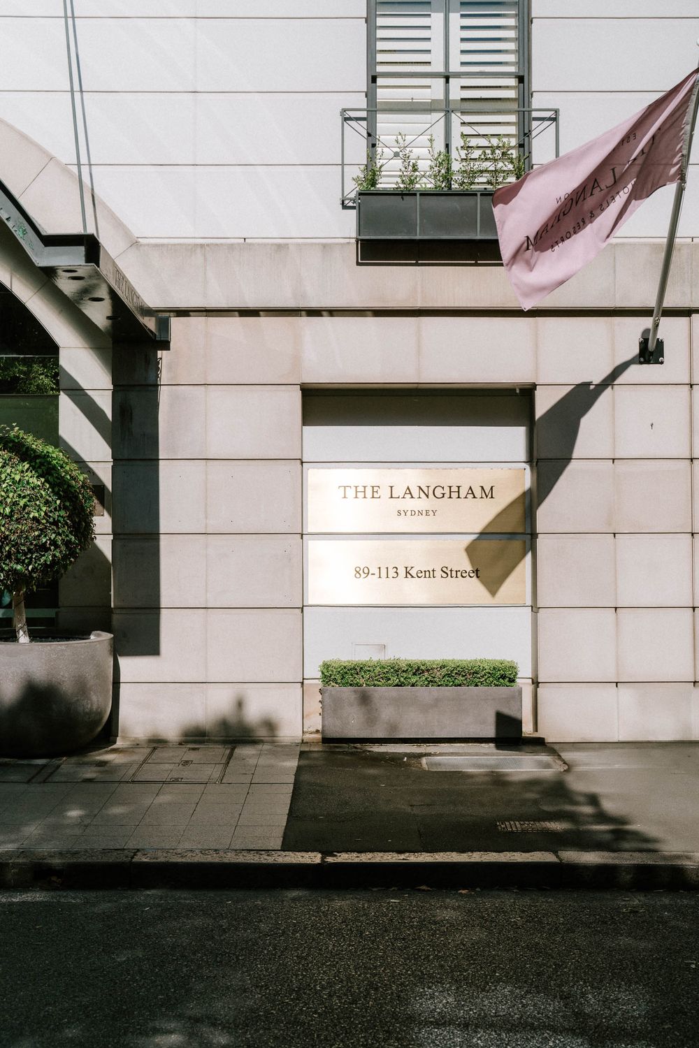 The Langham Sydney hotel entrance at 89-113 Kent Street, featuring elegant stone facade and manicured plants.