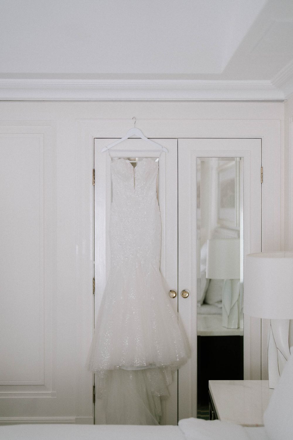 Elegant white lace mermaid wedding dress hanging on a hanger against white wardrobe doors in a bright bridal suite.