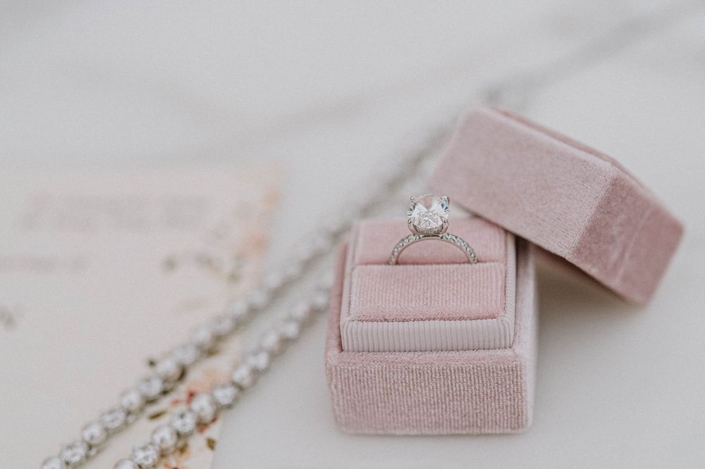 Diamond solitaire engagement ring displayed in an open pink velvet ring box on a marble surface.