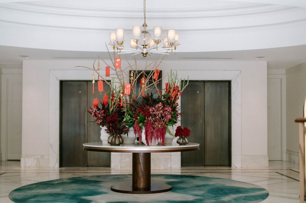 Elegant hotel lobby with a round marble table adorned with lush floral arrangements beneath a chandelier.