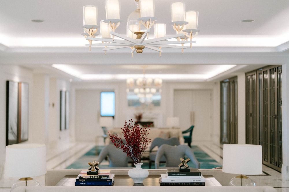 Elegant living room with gold chandelier, teal sofa, floral centerpiece, and soft white lighting in a luxury interior.