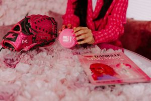 Pink baseball glove, Danielle Magazine, and pink accessories arranged on a fluffy pink surface.