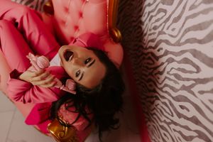 Woman in pink suit lying on zebra print surface holding pink perfume bottle.