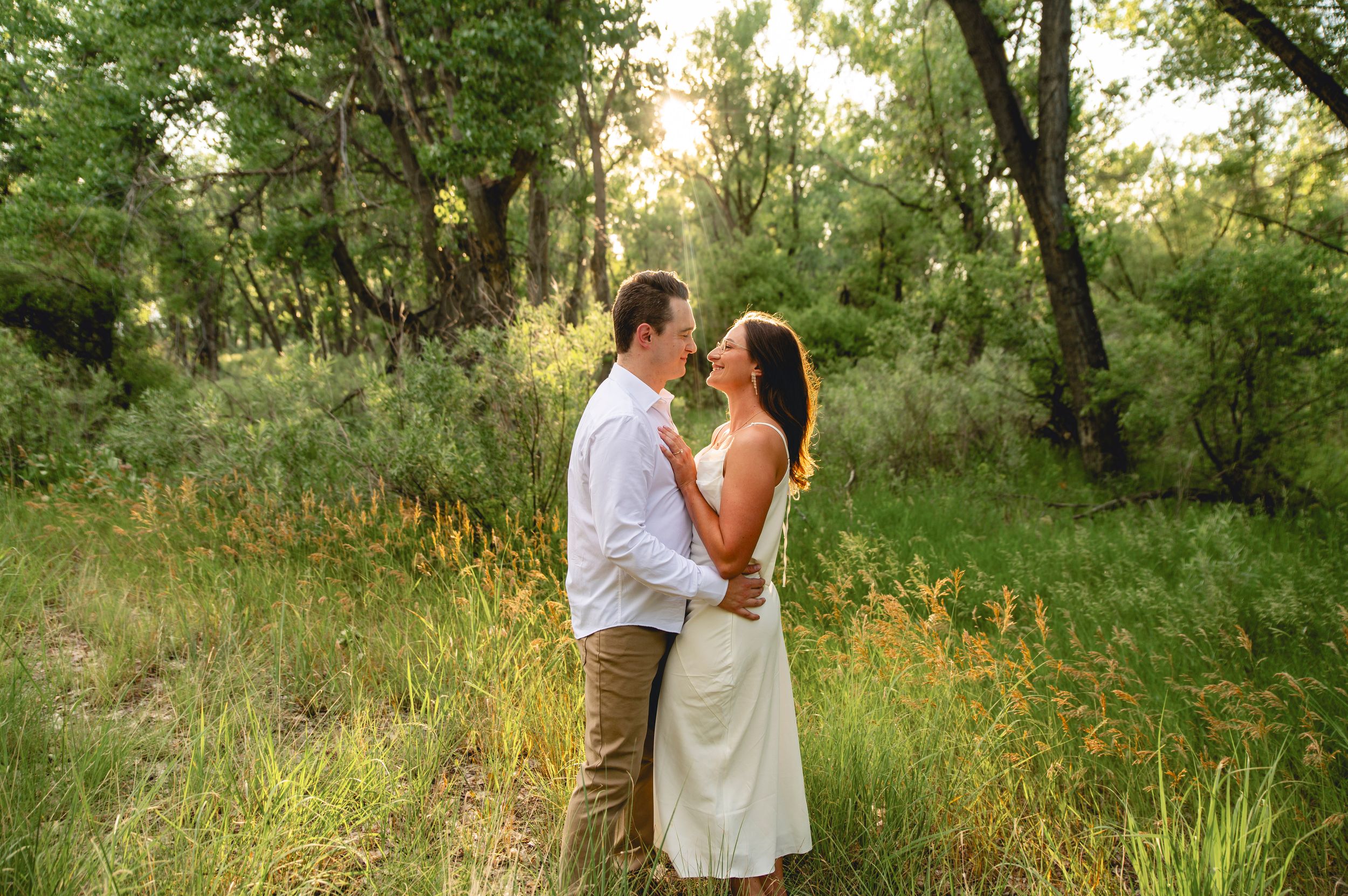 Couple embracing in a lush green meadow surrounded by trees during golden hour.