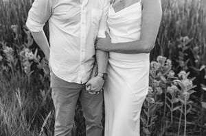 Black and white photo of a couple holding hands and embracing in a field of wildflowers.