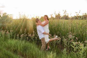 Couple embracing in a sunlit meadow with tall green grass and wildflowers during golden hour.